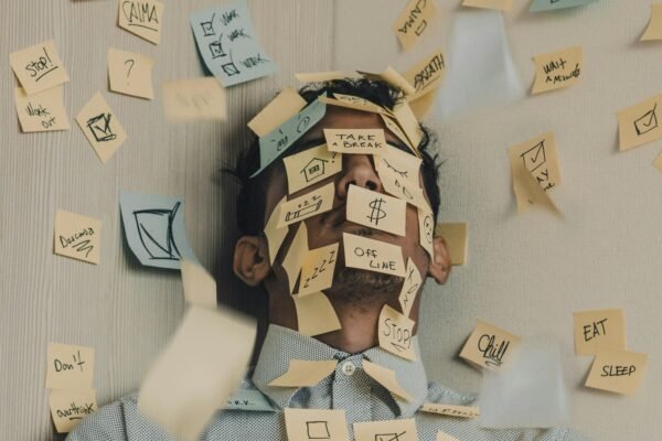 Man covered in sticky notes at office desk representing financial overwhelm