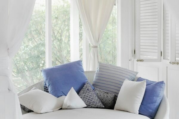 White cuddle chair with throw pillows near a window as a home decor accent