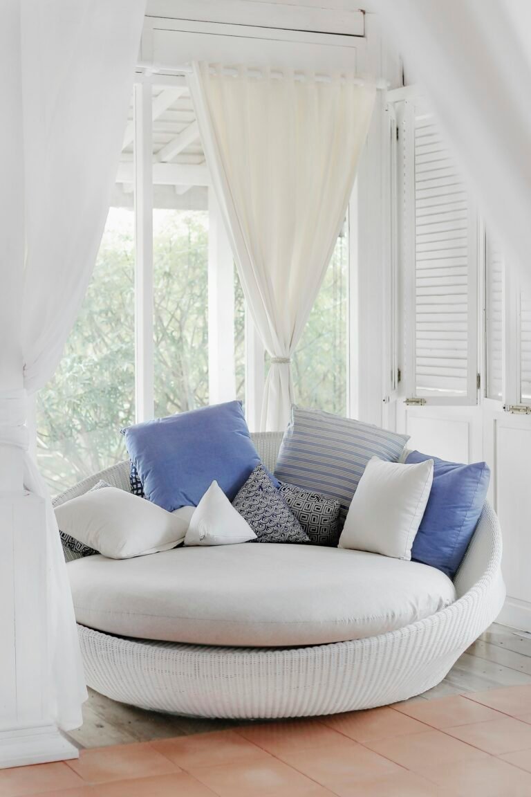White cuddle chair with throw pillows near a window as a home decor accent